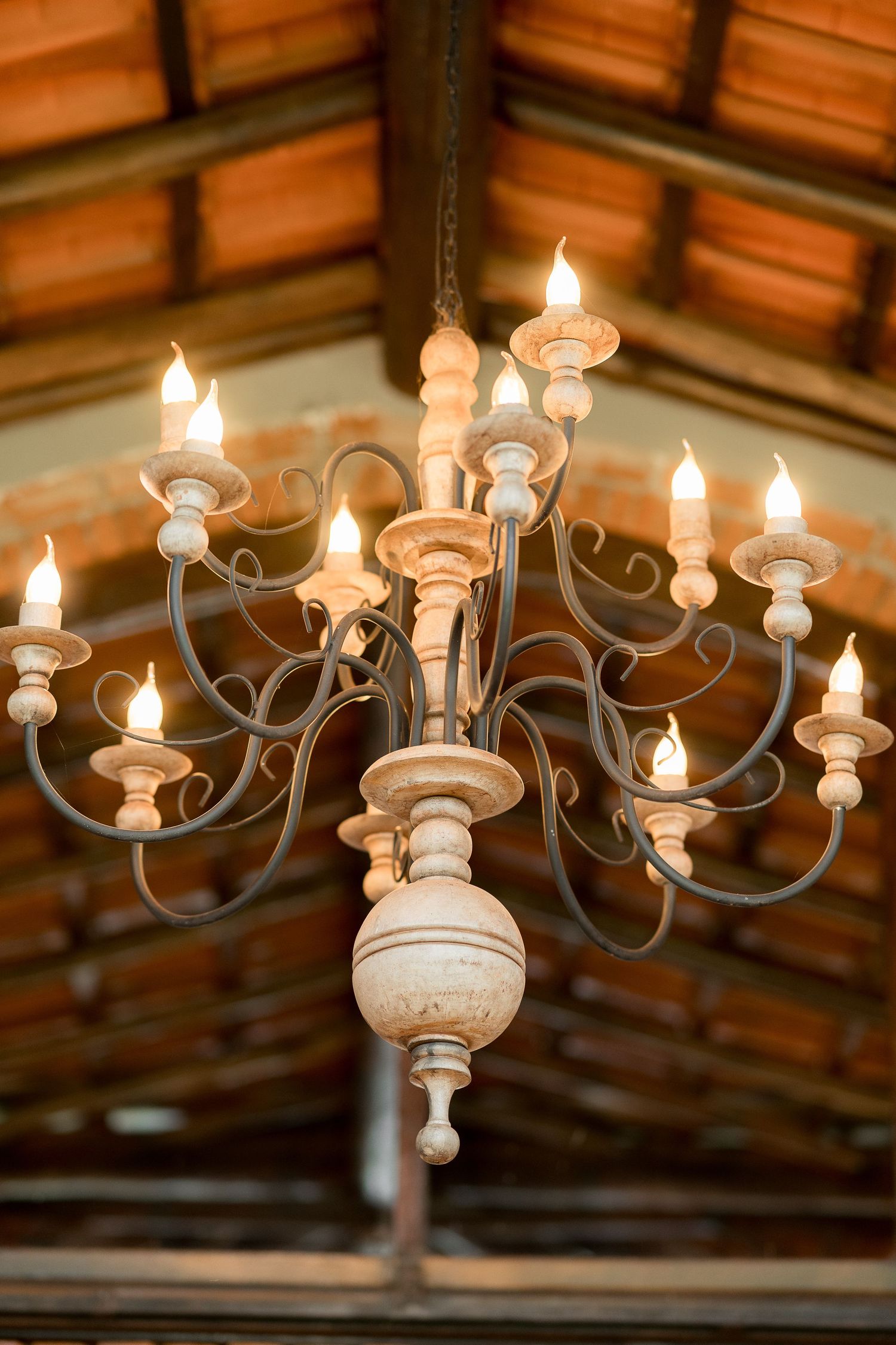 Rustic wooden and wrought iron chandelier with candle-style bulbs hanging from a wooden beamed ceiling.