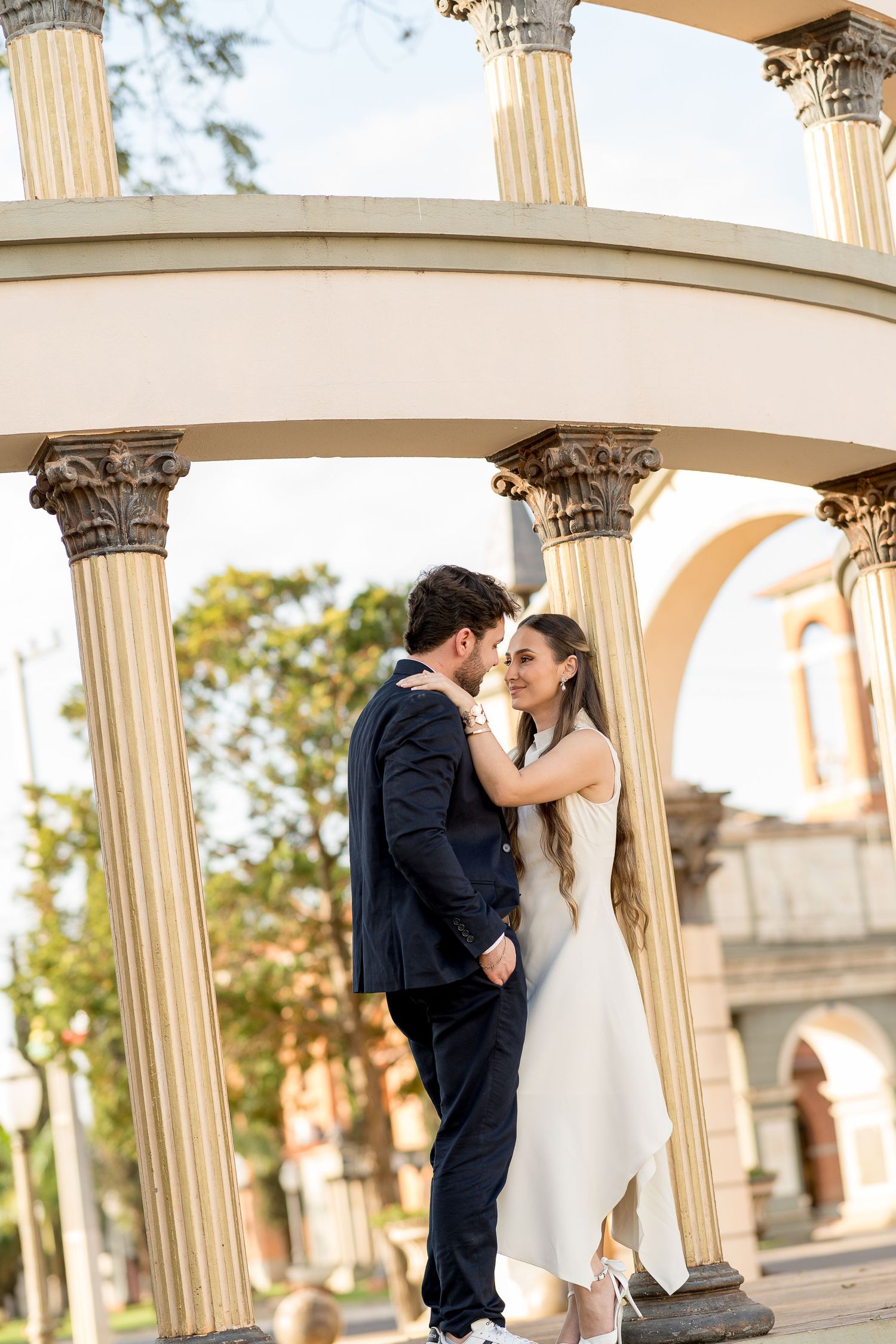 Couple in wedding attire embracing under elegant classical columns outdoors.