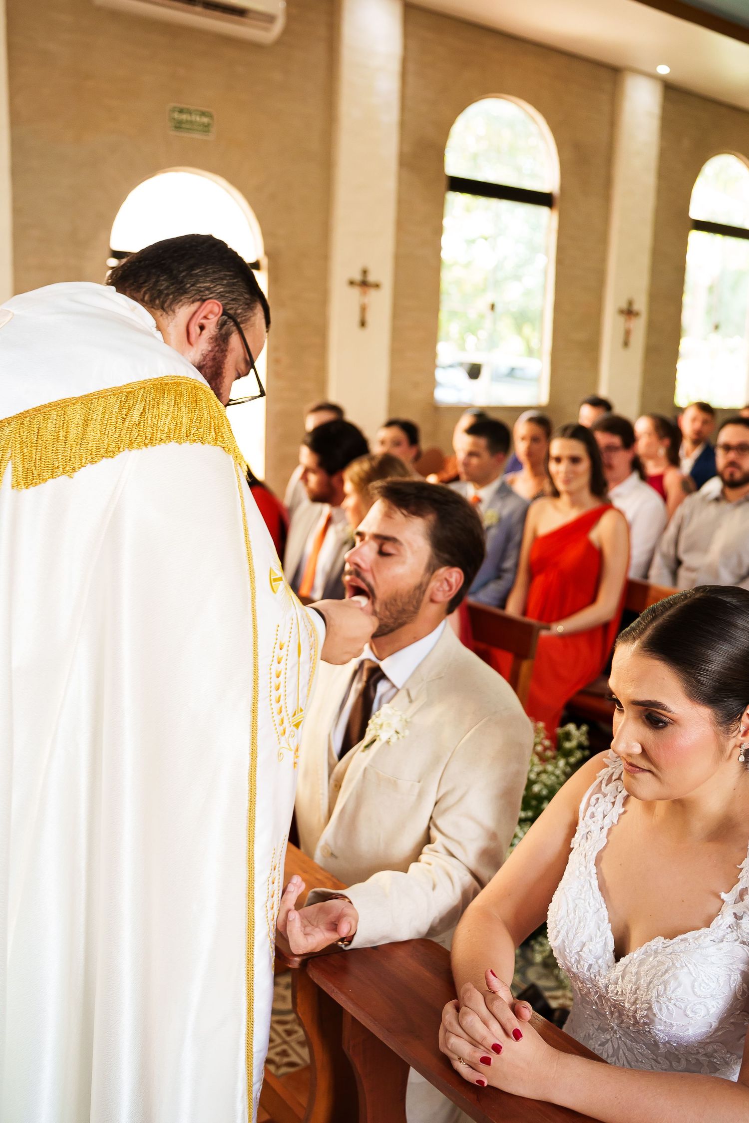 Bride and groom kneeling before a priest during a Catholic wedding ceremony in a church.