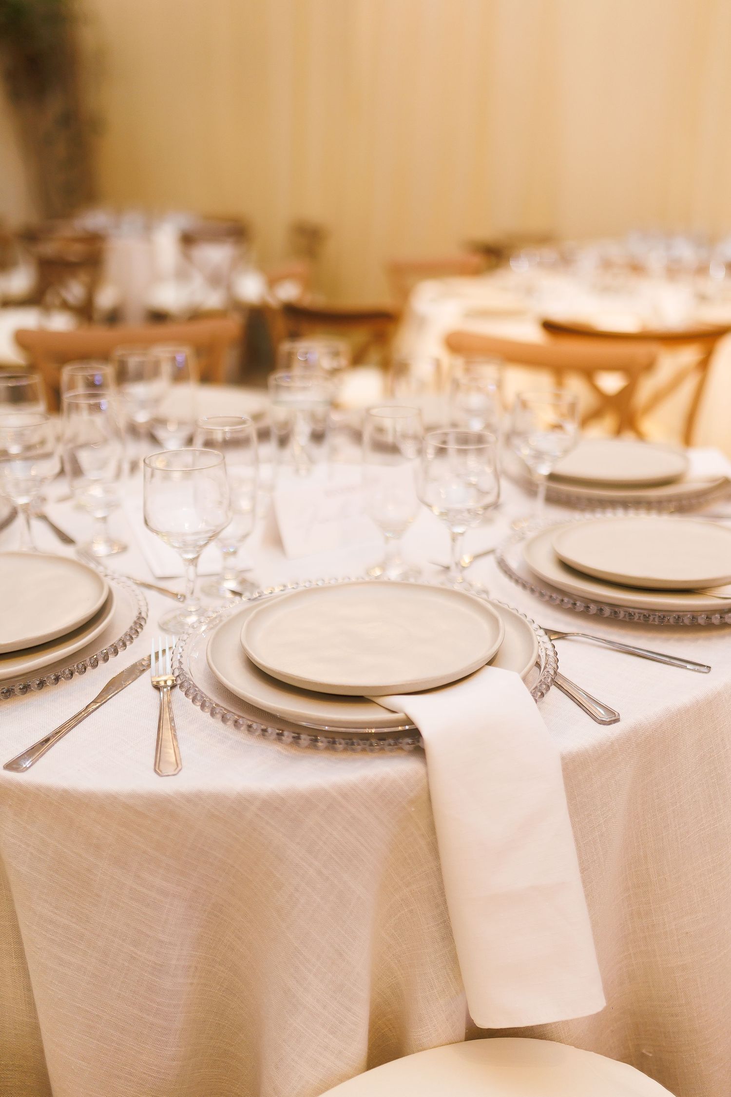 Elegant round banquet table set with cream linens, silver charger plates, white napkins, and crystal wine glasses.