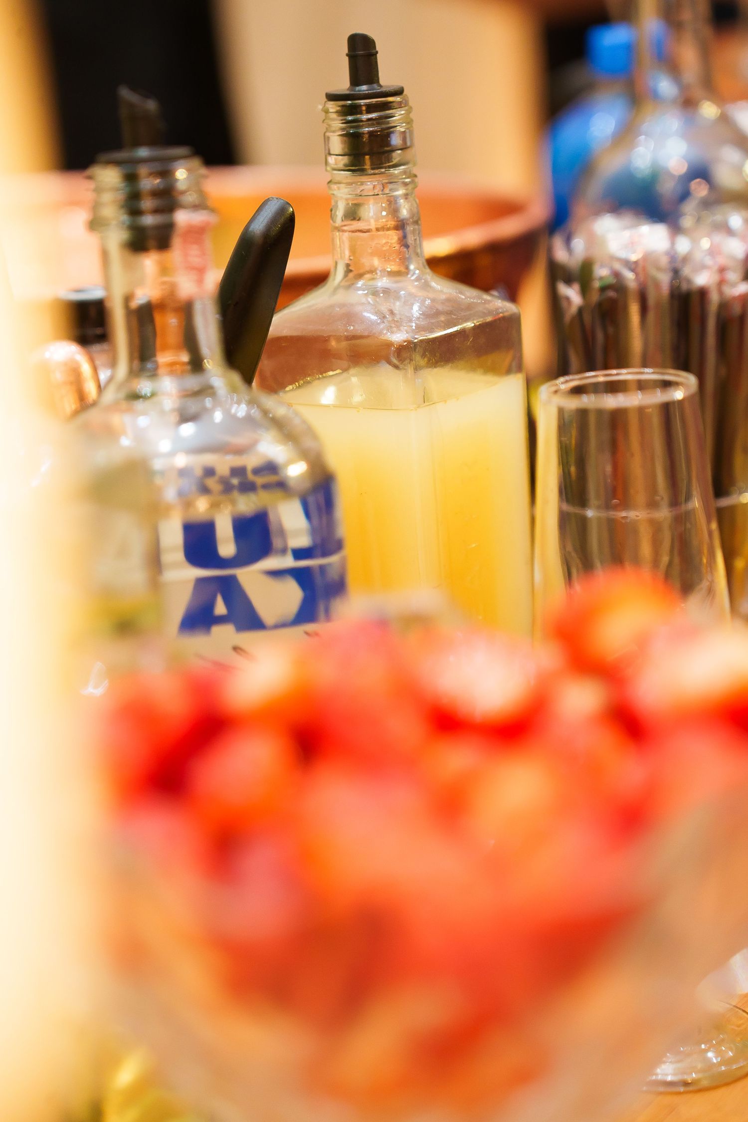 Vodka bottles and fresh strawberries displayed on a bar table with glasses and juice for cocktail mixing.