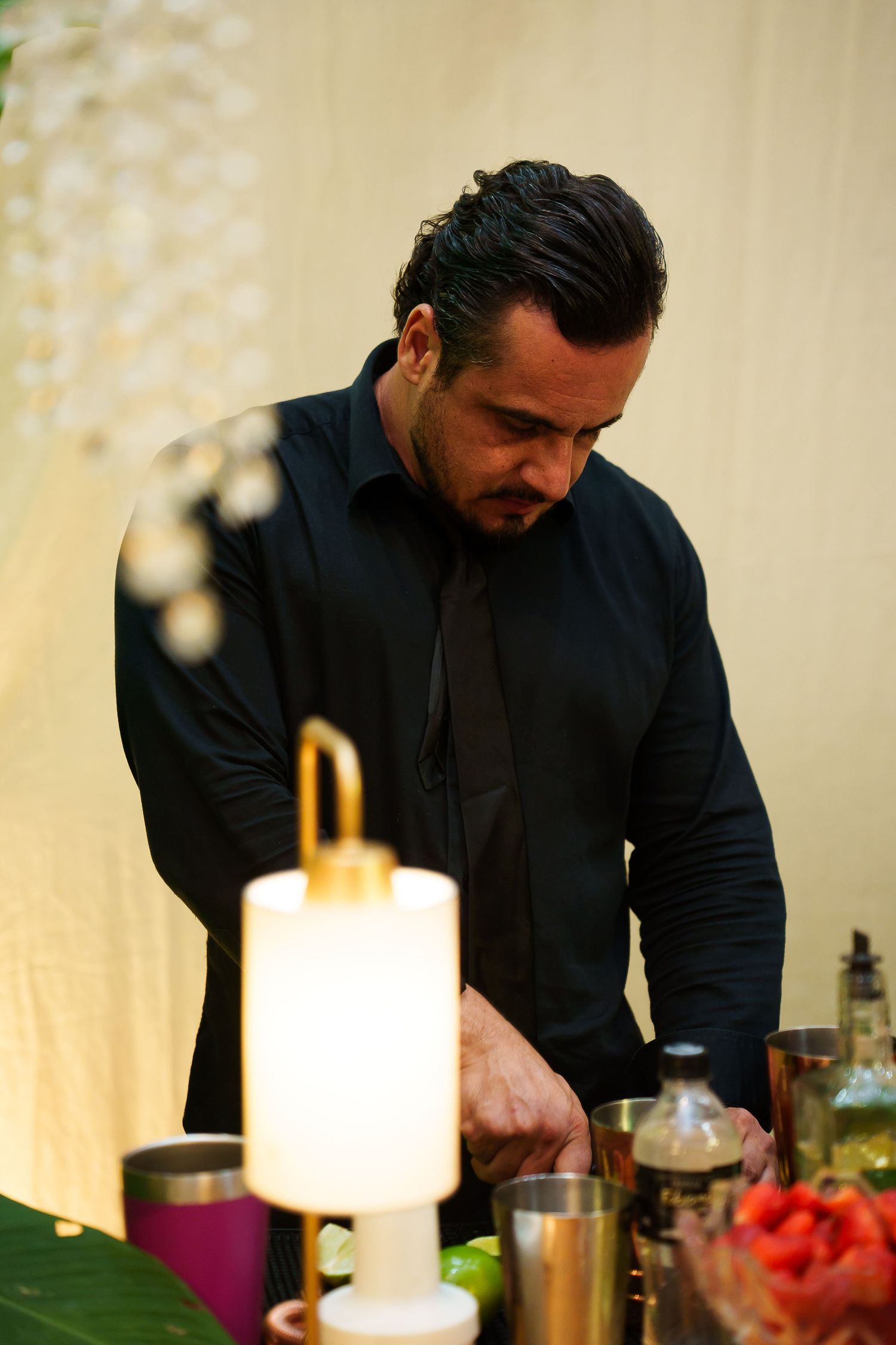 A bartender in a black shirt focuses on preparing cocktails at an elegantly decorated bar with gold accents and soft lighting.