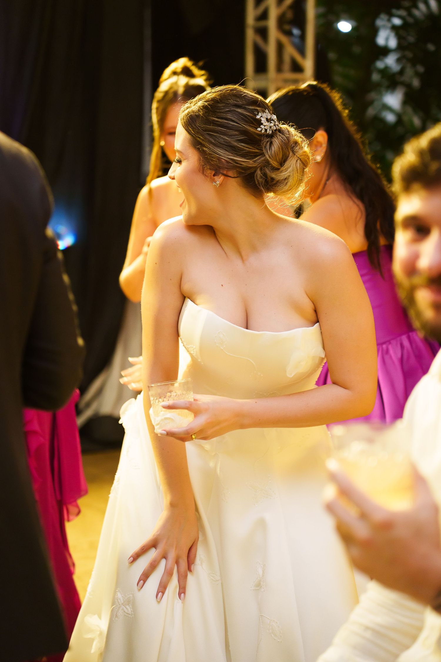 Bride in strapless white gown with updo hairstyle socializing at wedding reception with bridesmaids in pink dresses.