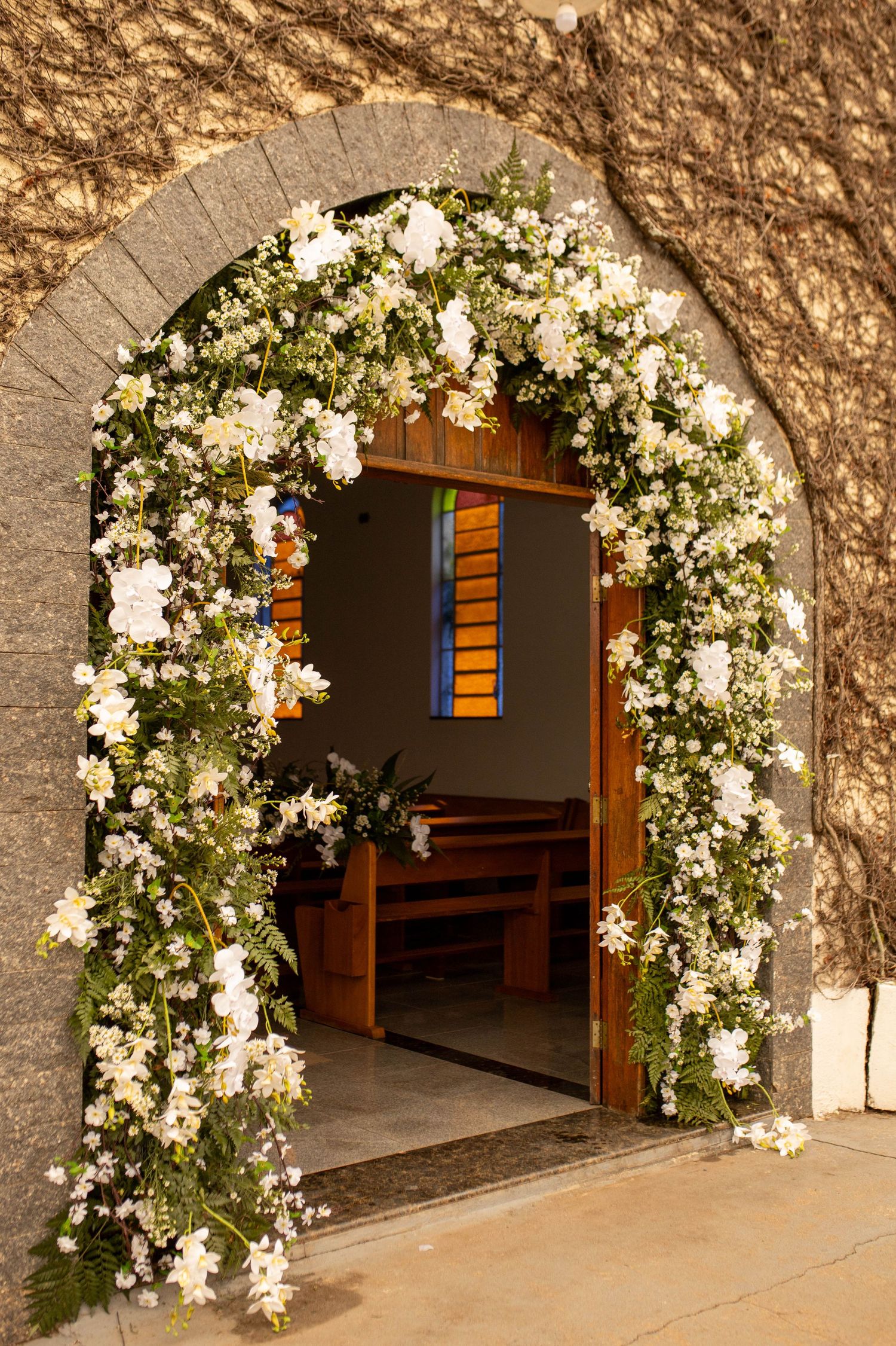 Church entrance arch adorned with white flowers and greenery, leading to wooden pews and stained glass windows inside.