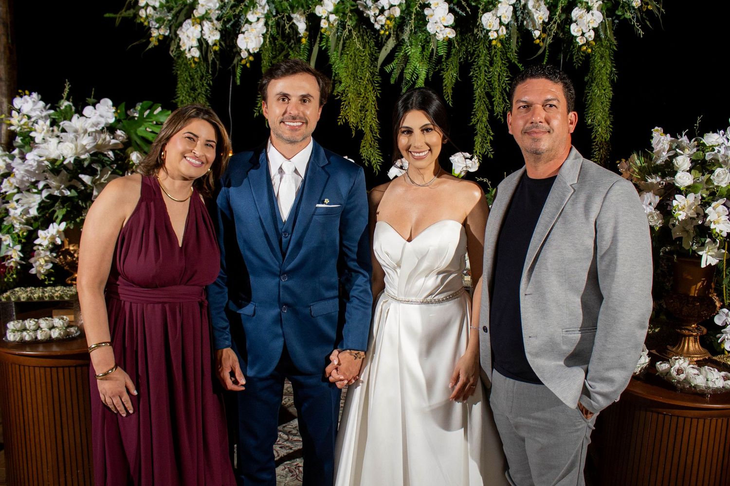 A bride and groom pose with family members at an elegant wedding reception decorated with white flowers.