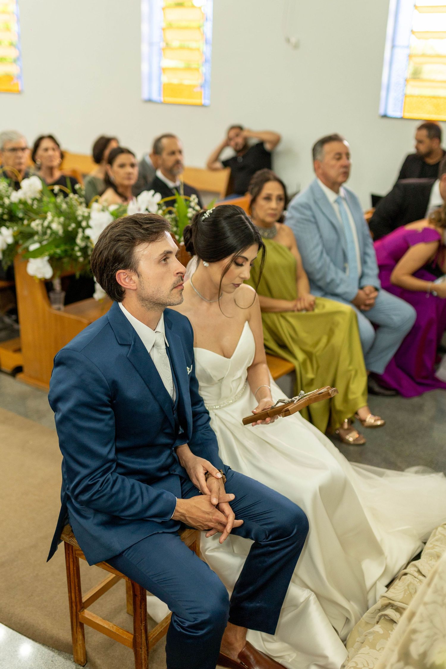 Bride and groom sit together at church altar during wedding ceremony, guests seated in pews behind them.