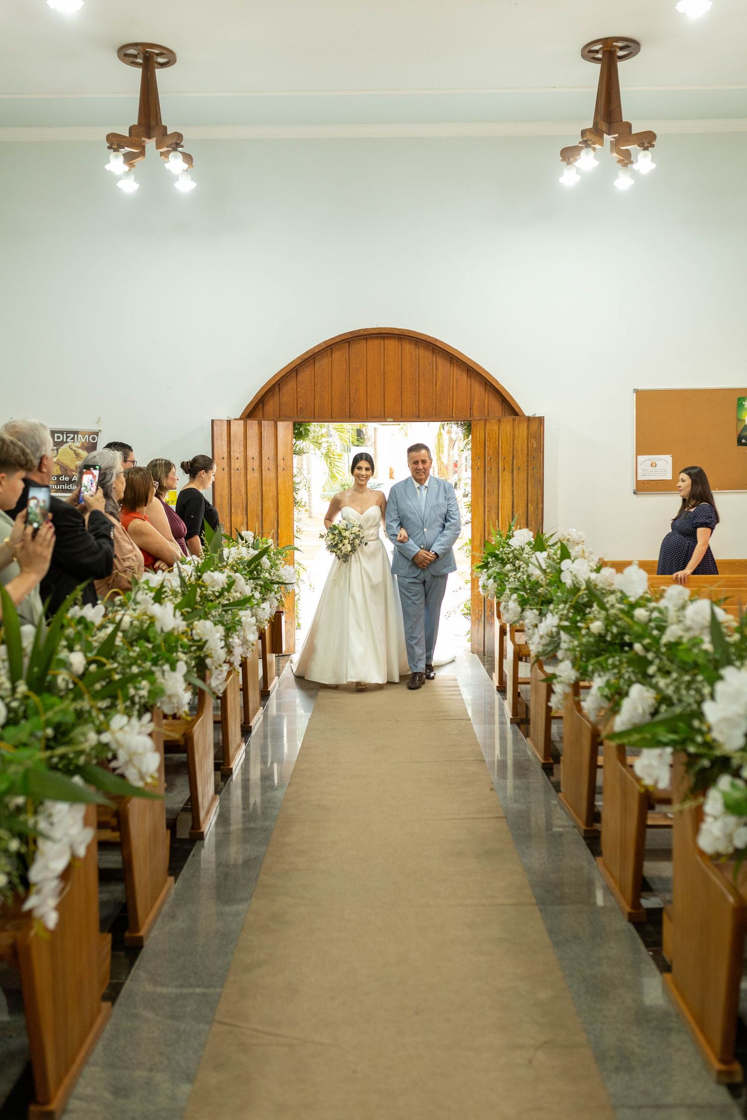Bride and groom walking down the aisle in a white church decorated with white floral arrangements on wooden pews.