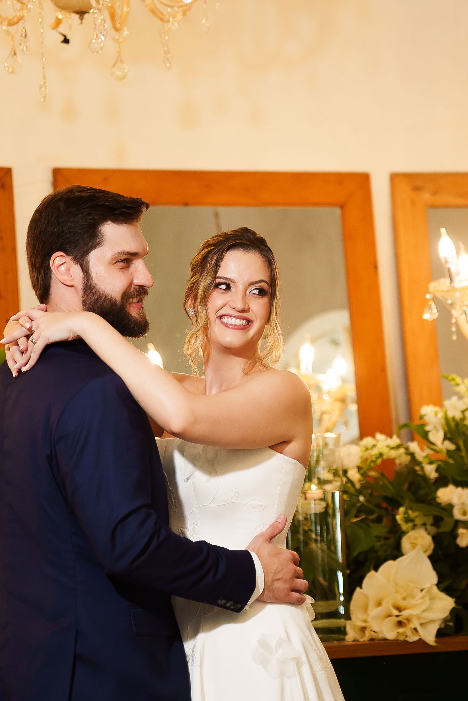 Bride and groom share first dance at elegant wedding reception, bride smiling in white gown, groom in navy suit.