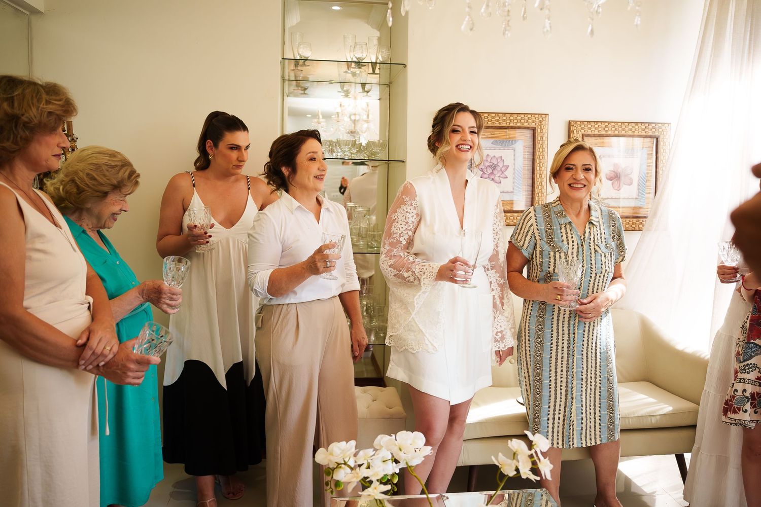 Group of elegantly dressed women socializing indoors at a bridal gathering, holding drinks and smiling.