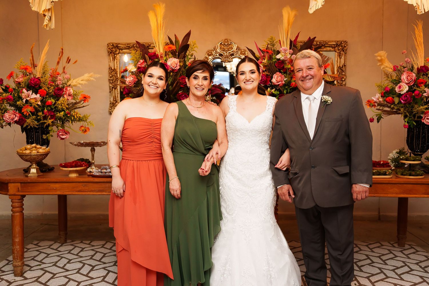 Bride in white gown poses with family members in formal attire at elegant wedding reception with floral arrangements.