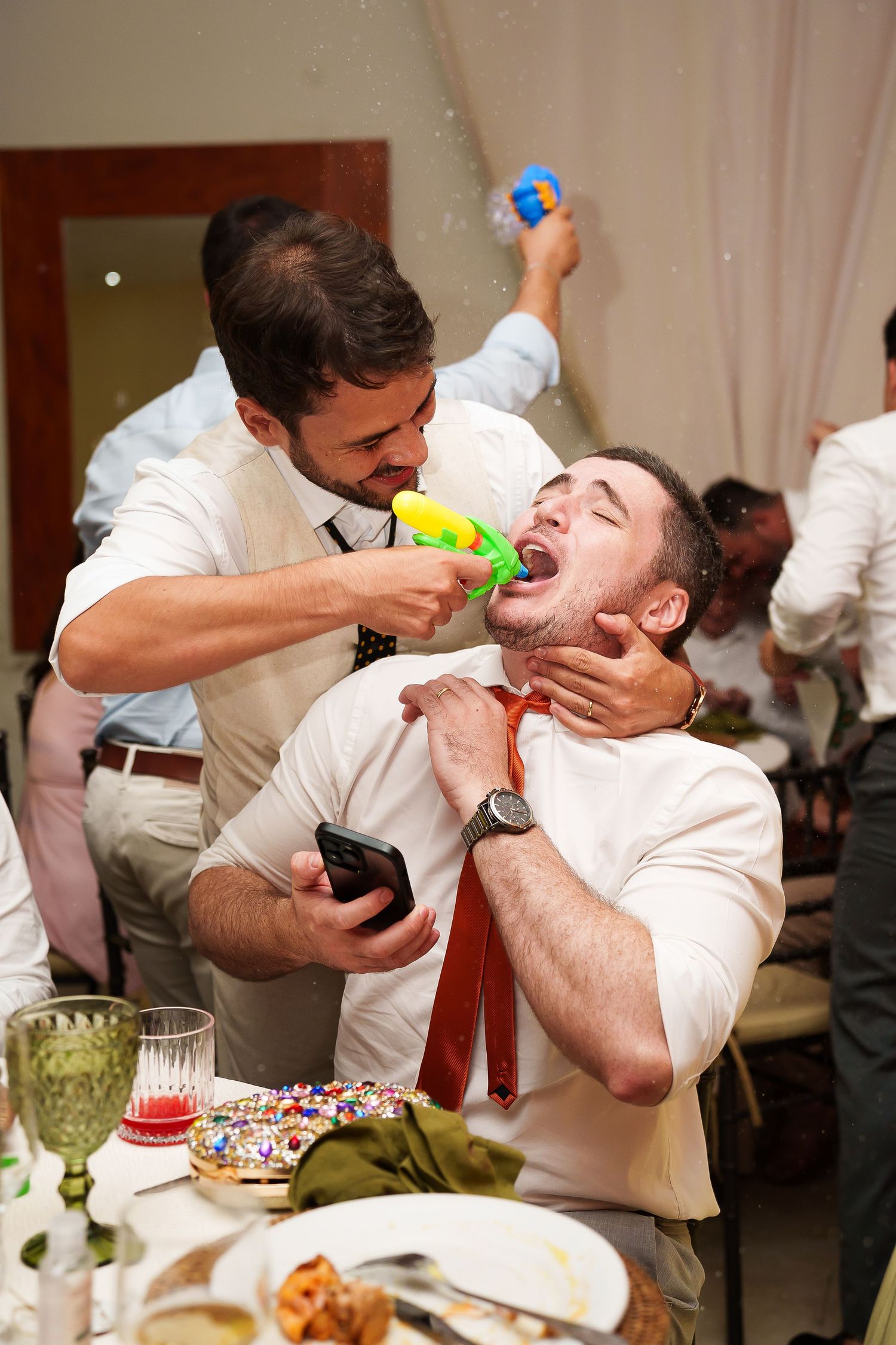 Two men in white shirts playing with a water gun at a party celebration dinner event.