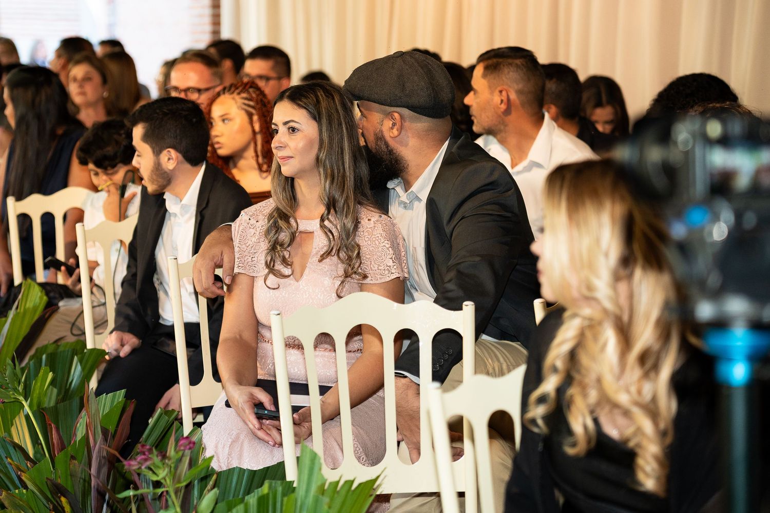 Guests seated in white chairs at an elegant indoor event, attentively watching a ceremony or presentation.