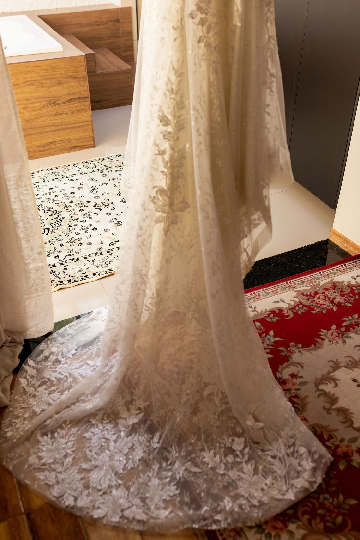Elegant white lace wedding dress with floral appliques displayed hanging, showcasing its long train on hardwood floor.