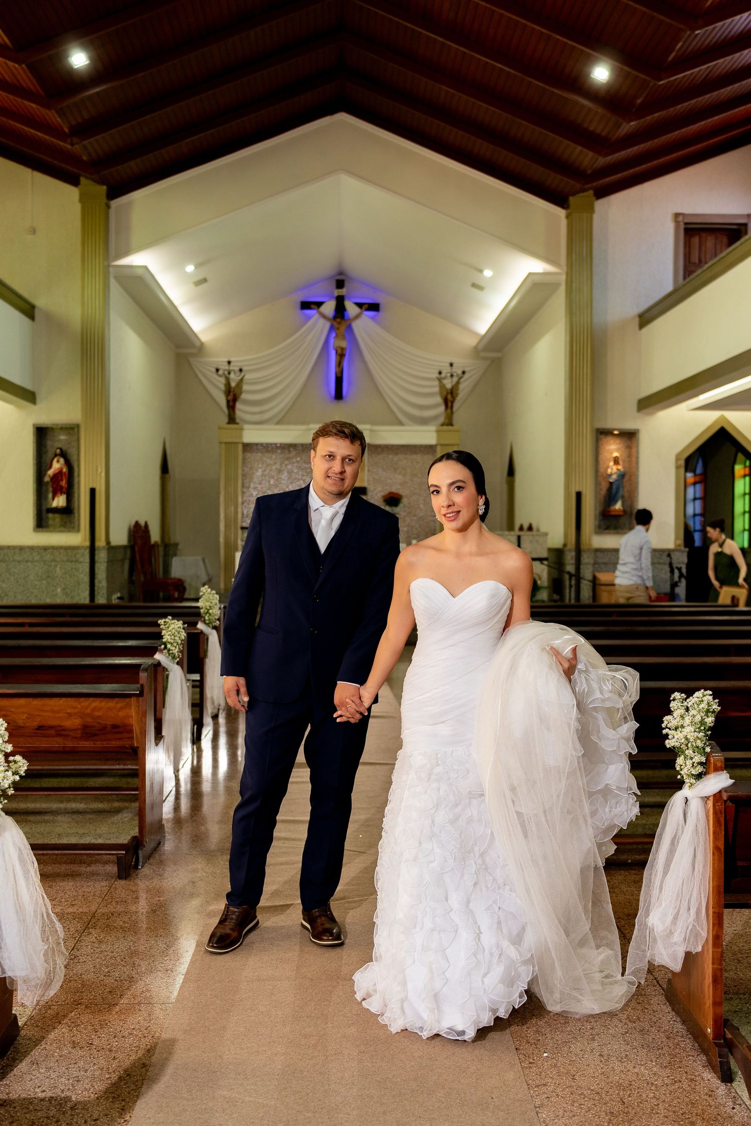 Bride and groom walk hand in hand down the aisle of a decorated church after their wedding ceremony.