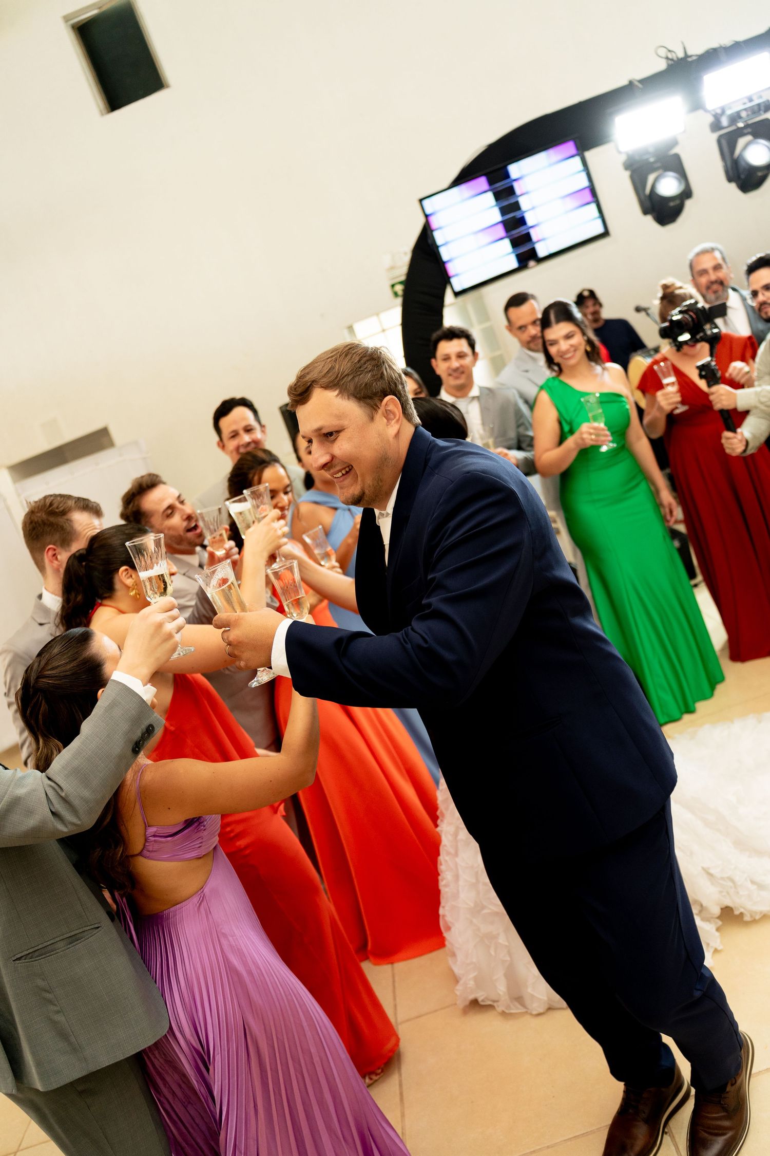Guests celebrating at a wedding reception, dancing and toasting with champagne glasses in colorful formal attire.