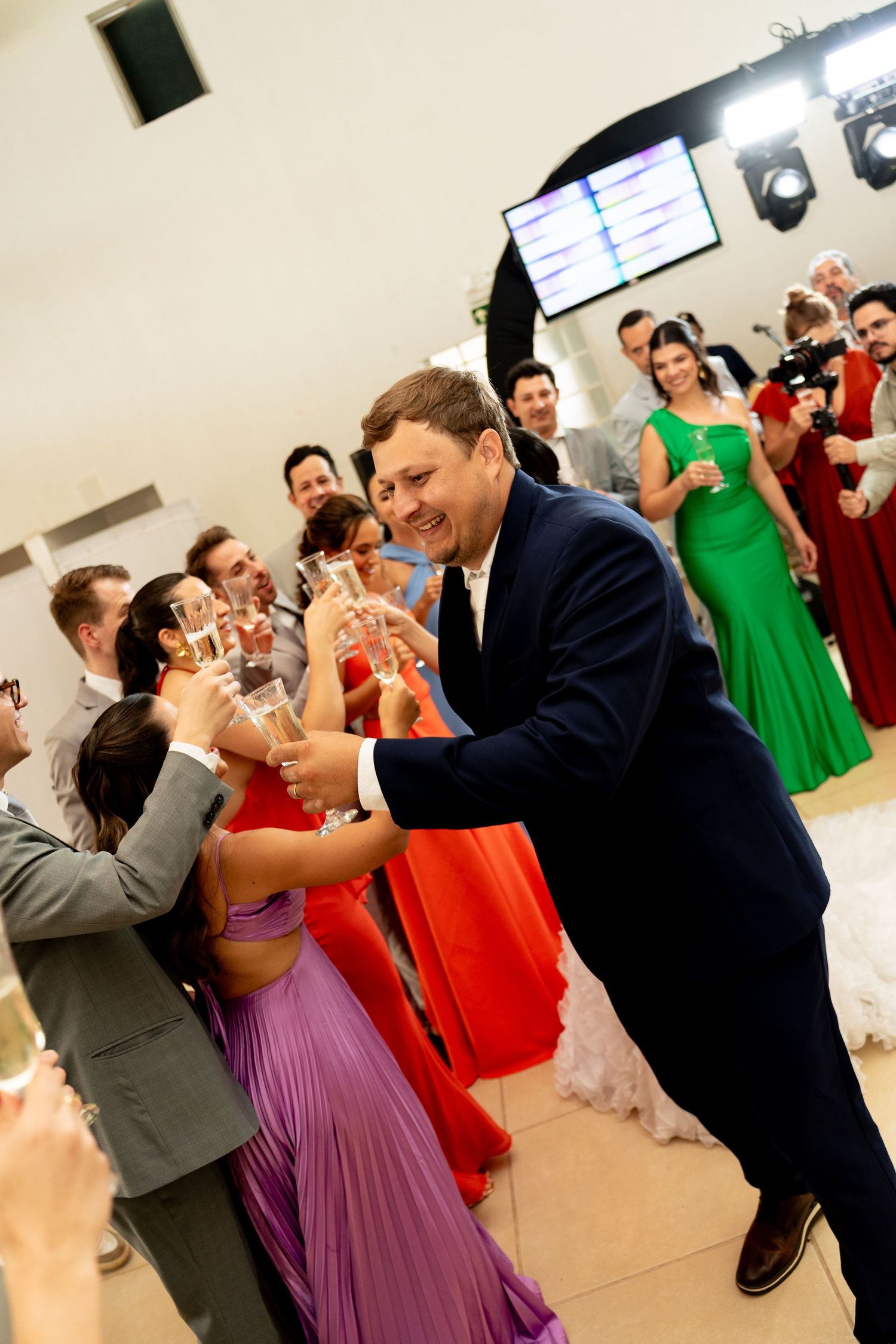 Man in navy suit toasting champagne glasses with guests at elegant wedding reception celebration.