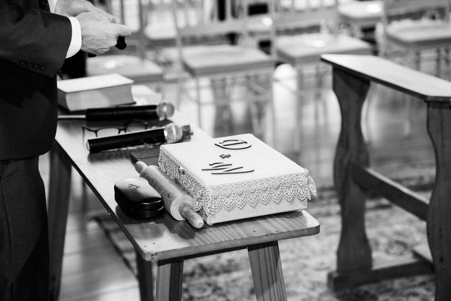 Black and white photo of a wedding cake on a wooden table with a groom standing nearby in a formal suit.