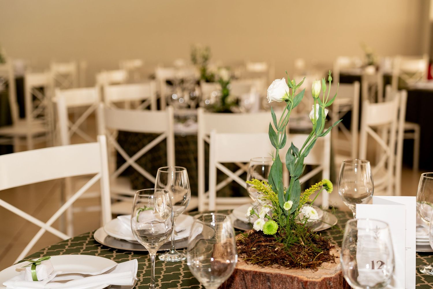 Elegant wedding reception table with white tulip centerpiece on wood slice, green runner, and crystal glassware.
