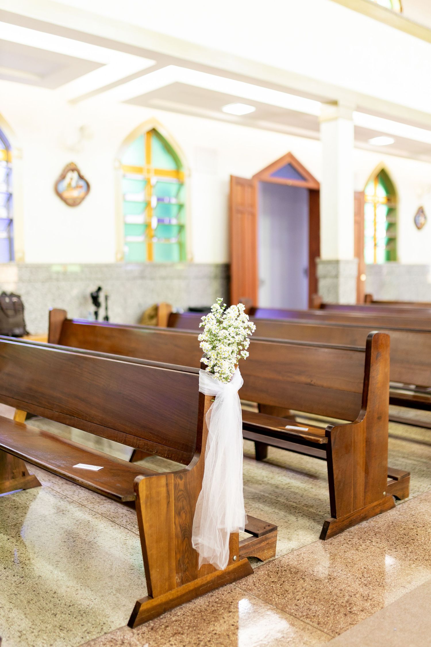 Church pews decorated with white tulle and baby's breath flowers for an elegant wedding ceremony.
