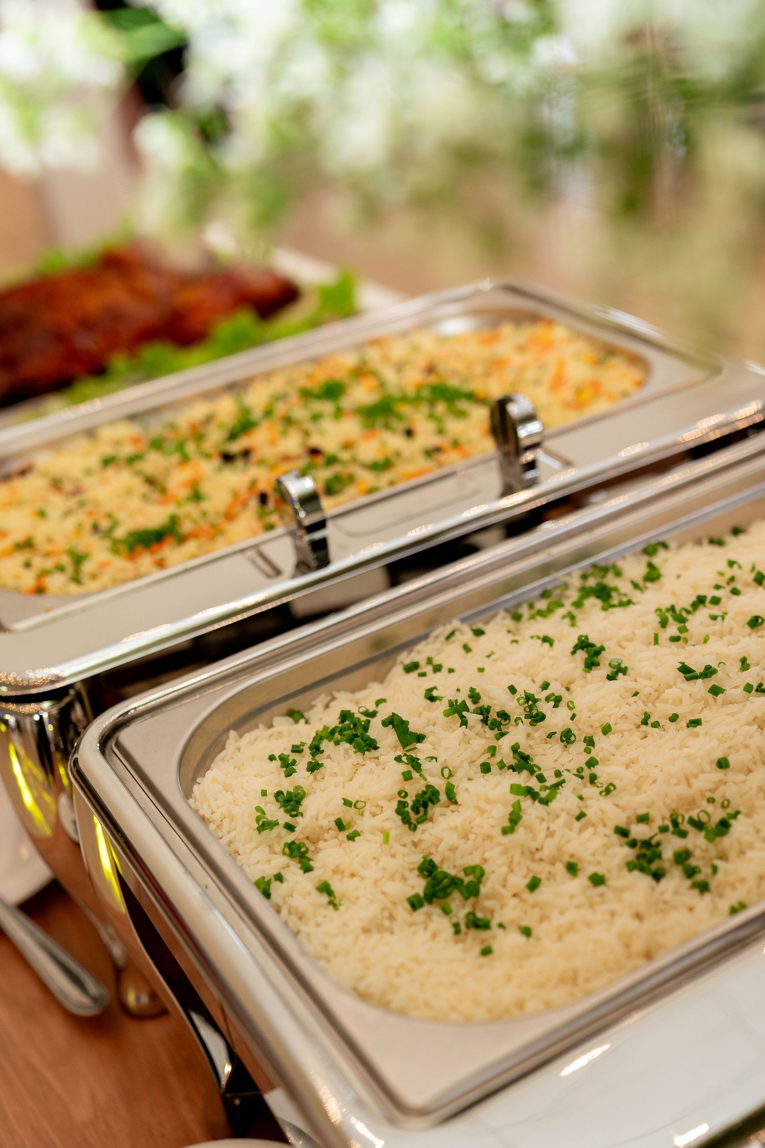 Two silver chafing dishes filled with seasoned rice garnished with fresh parsley at a buffet catering event.