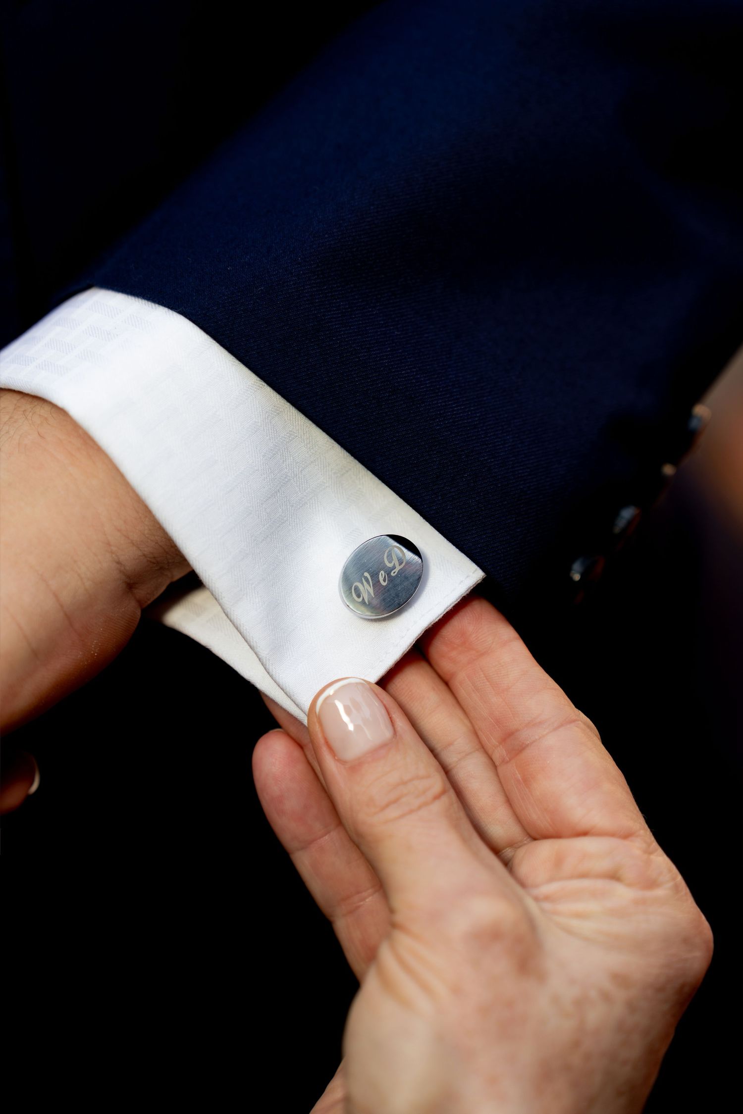Close-up of a personalized silver cufflink on a white dress shirt sleeve, held by a woman's hand.