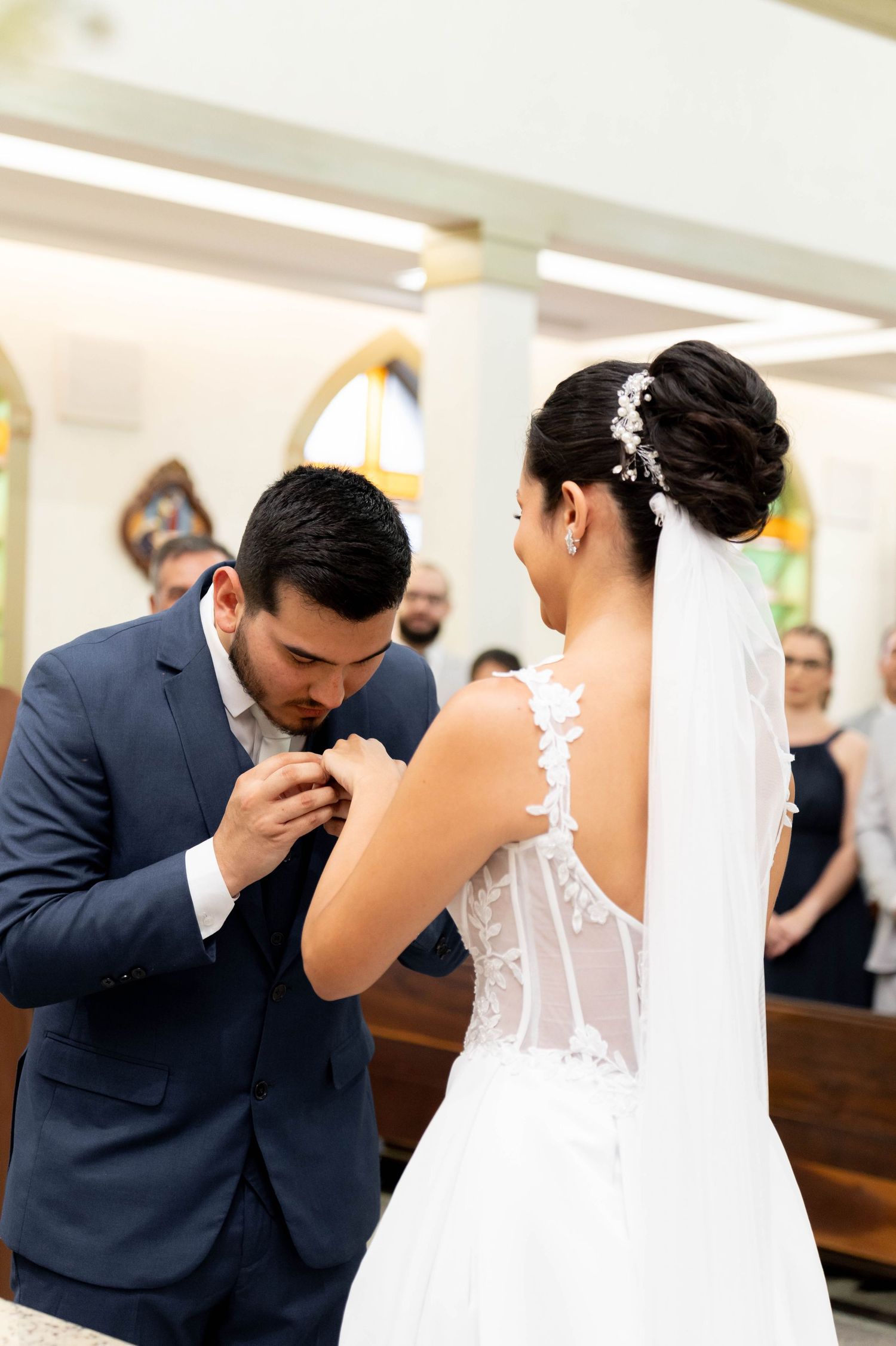 Groom in blue suit kissing bride's hand during wedding ring exchange ceremony in a church.