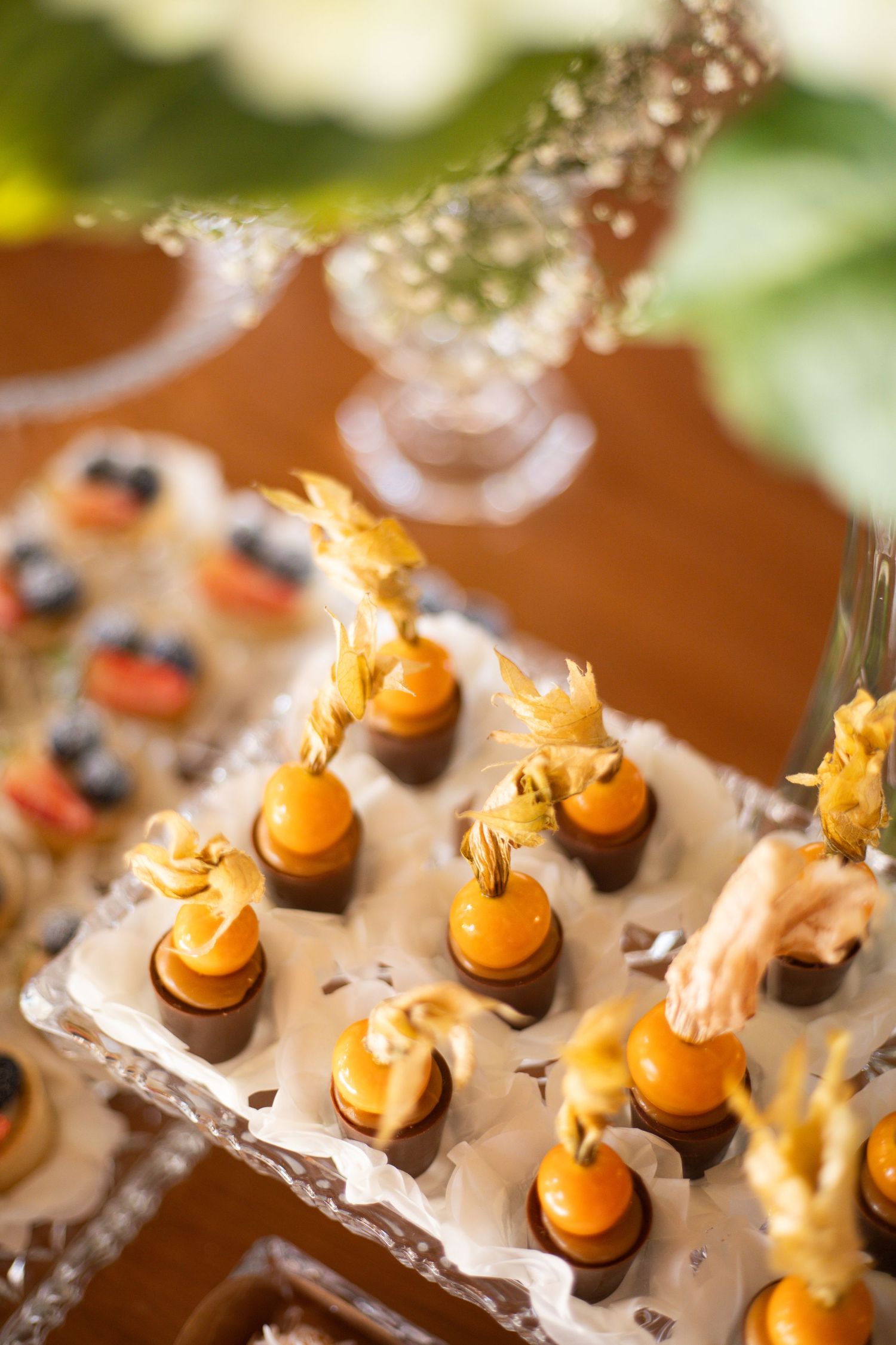 Elegant orange chocolate bonbons topped with delicate edible gold flowers arranged on a decorative silver tray at a catered event.