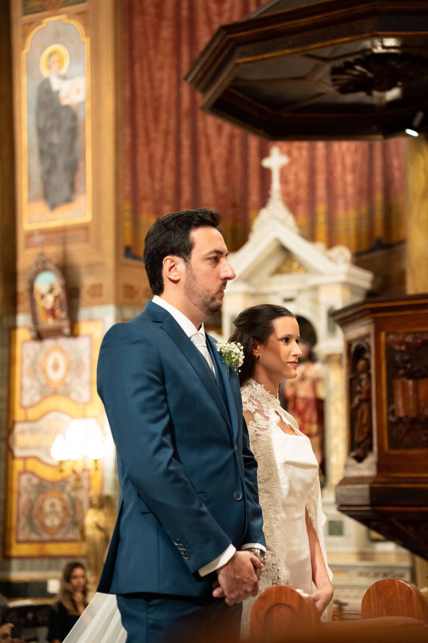 Bride and groom standing together at the altar during a church wedding ceremony, man in blue suit, woman in white lace gown.