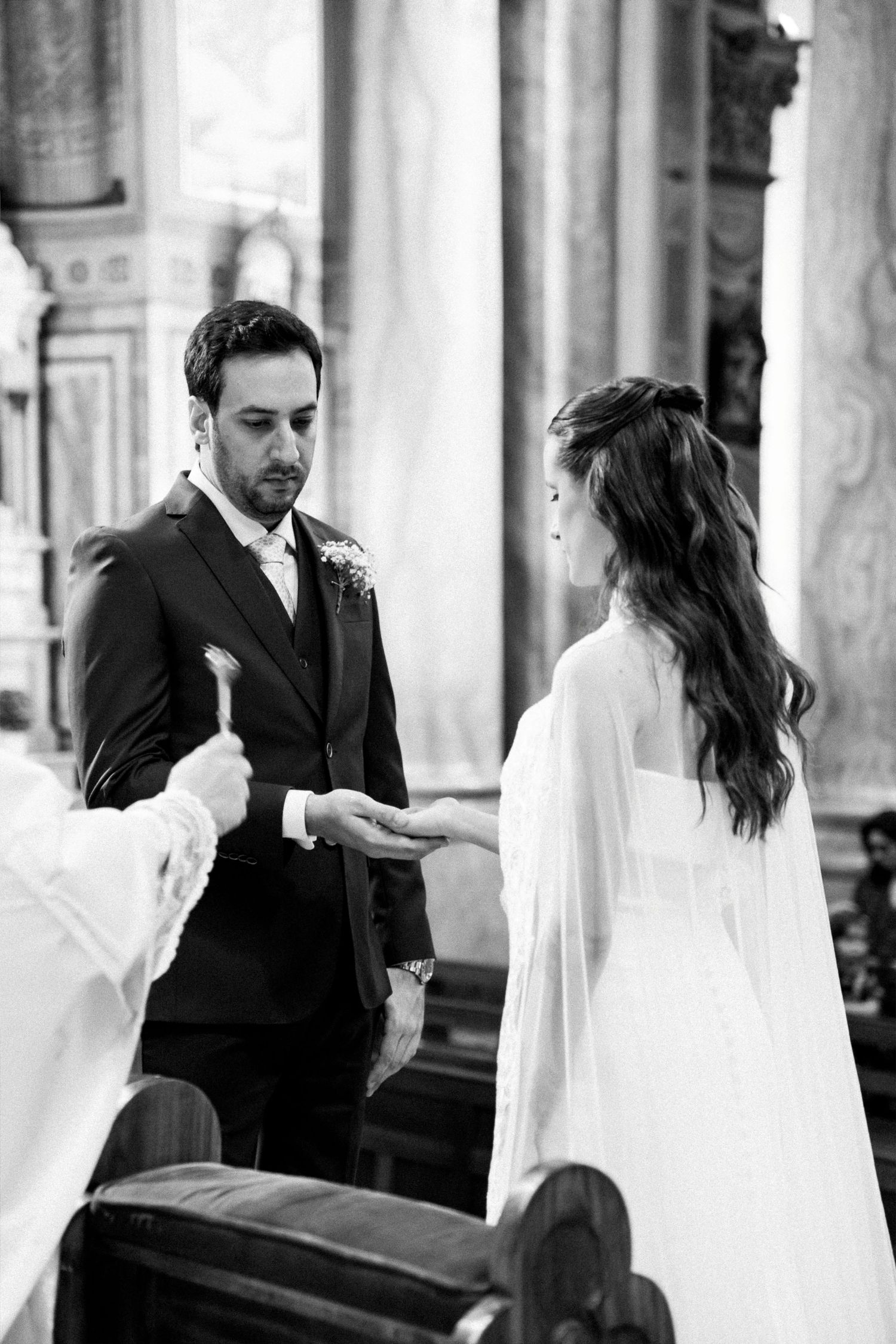 Black and white photo of a groom exchanging vows with his bride during a church wedding ceremony.