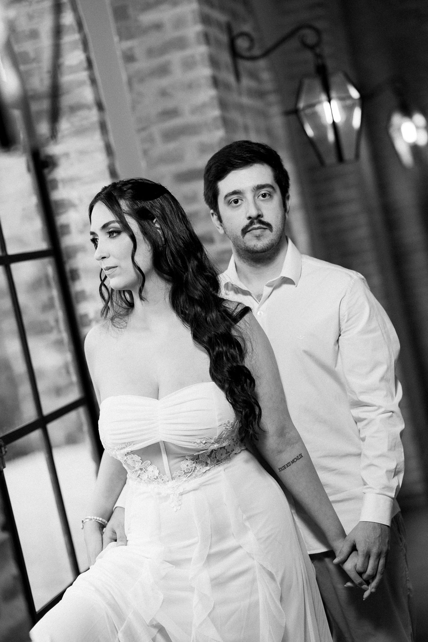 Black and white photo of a bride in strapless gown and groom in white shirt holding hands at elegant venue.