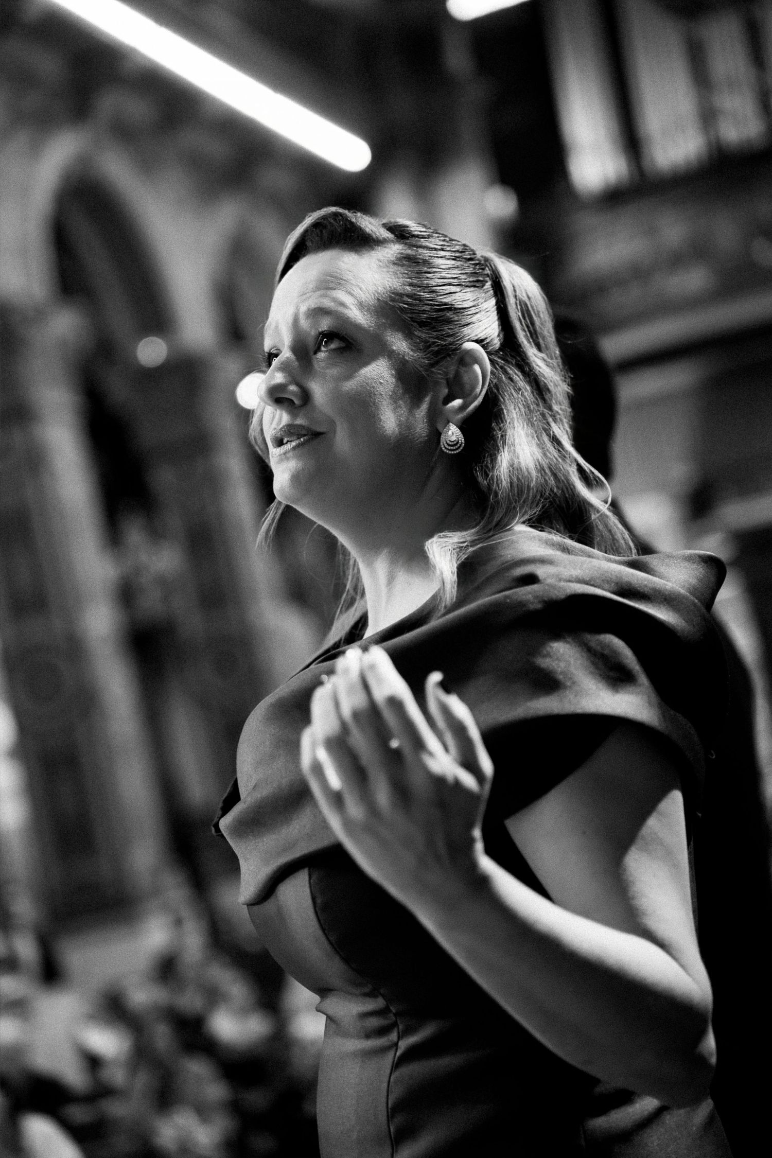 Elegant woman in black dress gazing upward in a dramatic black and white architectural setting.