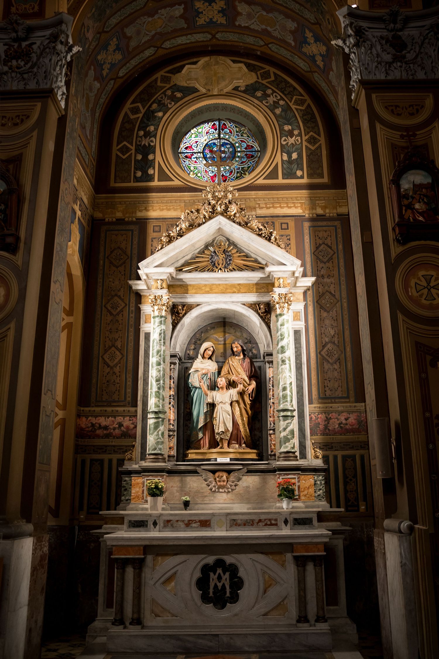Ornate Catholic church altar with Holy Family statue, gilded architecture, and stained glass rose window above.