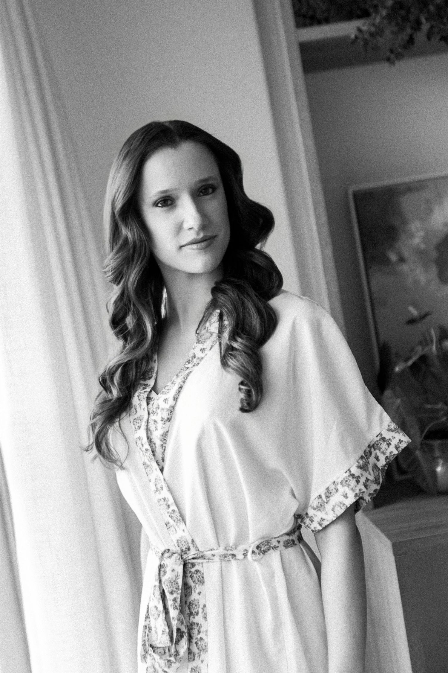 Black and white portrait of a woman in a floral-trimmed robe with elegant wavy hair, posing indoors.