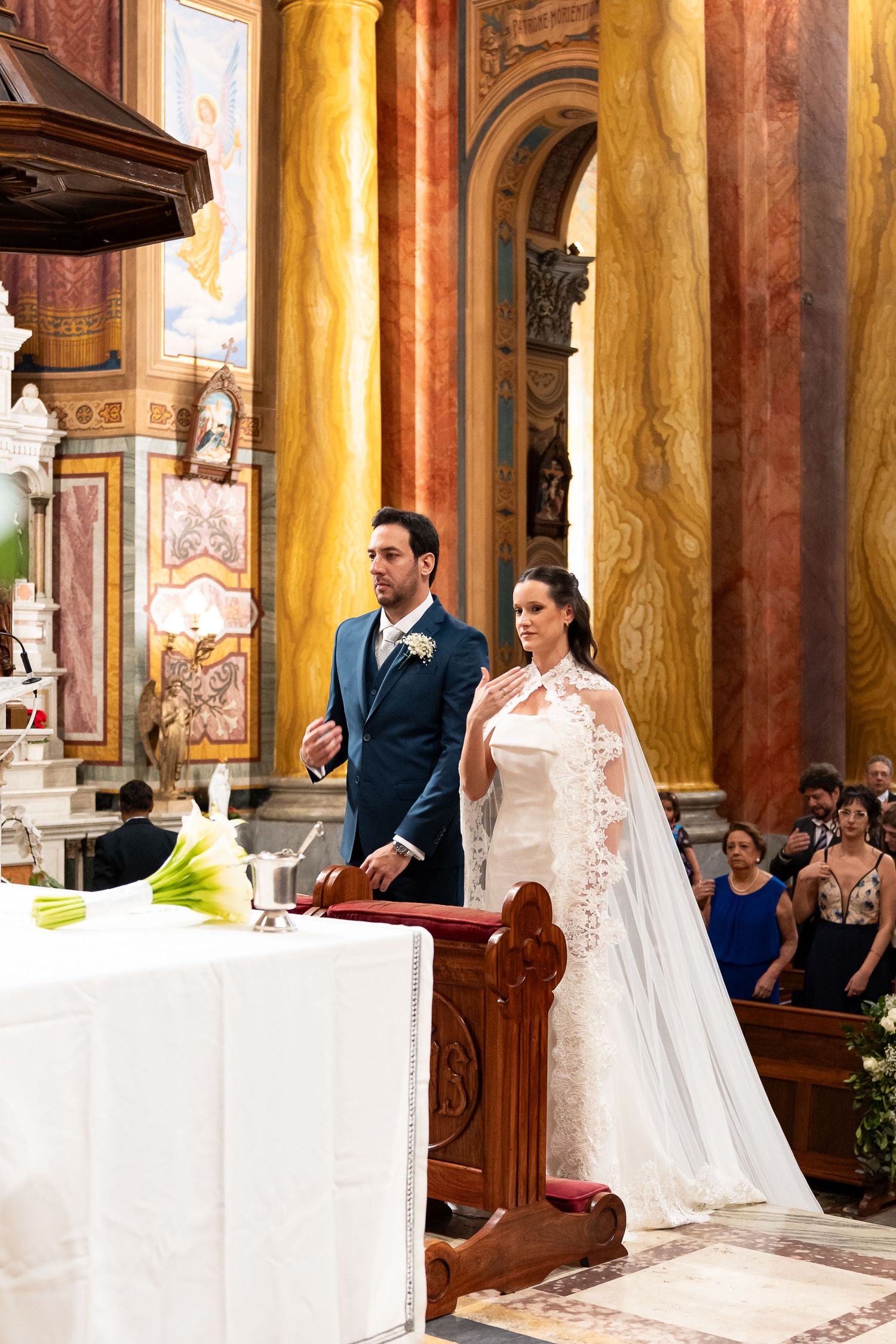 Bride and groom stand at the altar during a wedding ceremony in an ornate church with marble columns.