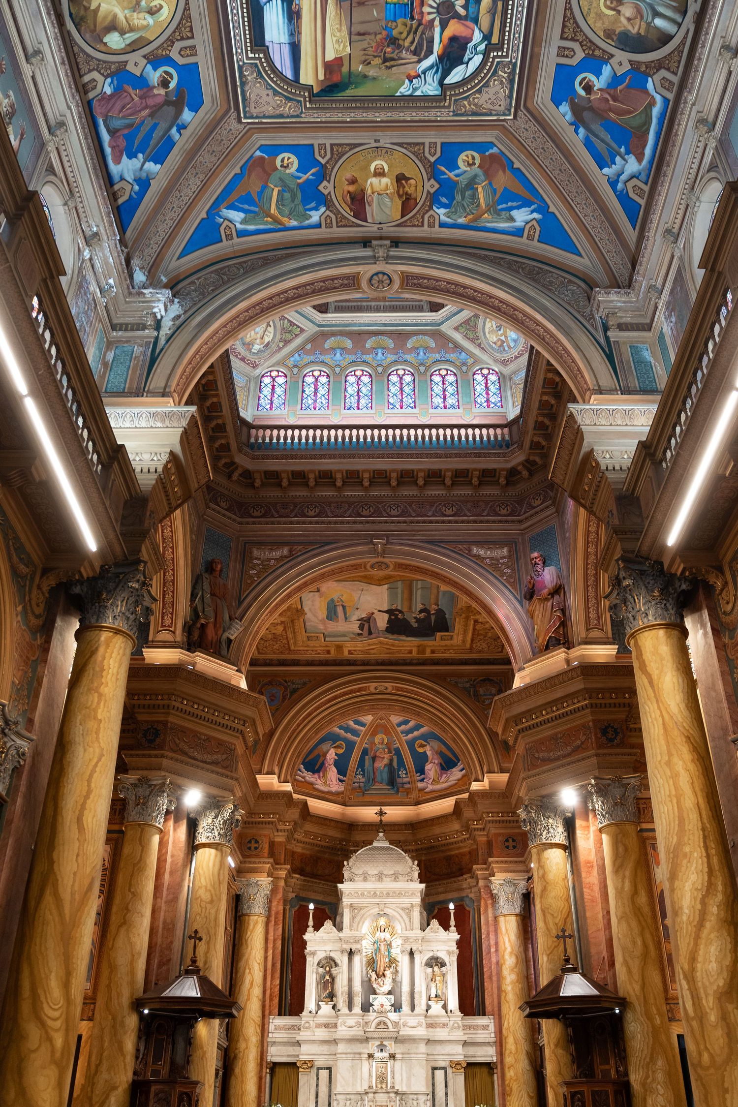 Ornate Catholic church interior with gilded ceiling murals, marble altar, and colorful frescoes under arched vaults.
