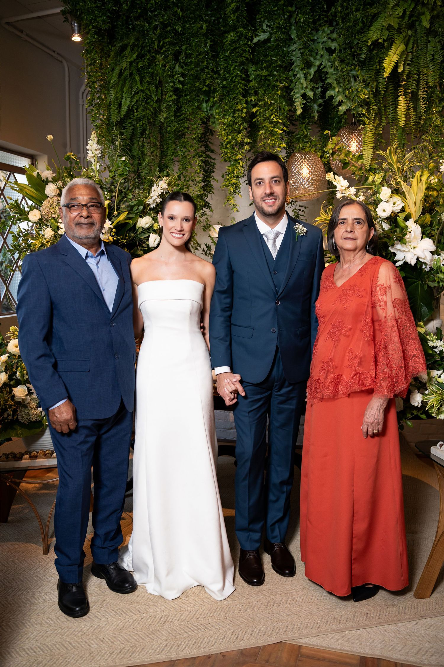 Wedding party of four posing together, bride in white gown, groom in navy suit, flanked by family in formal attire.