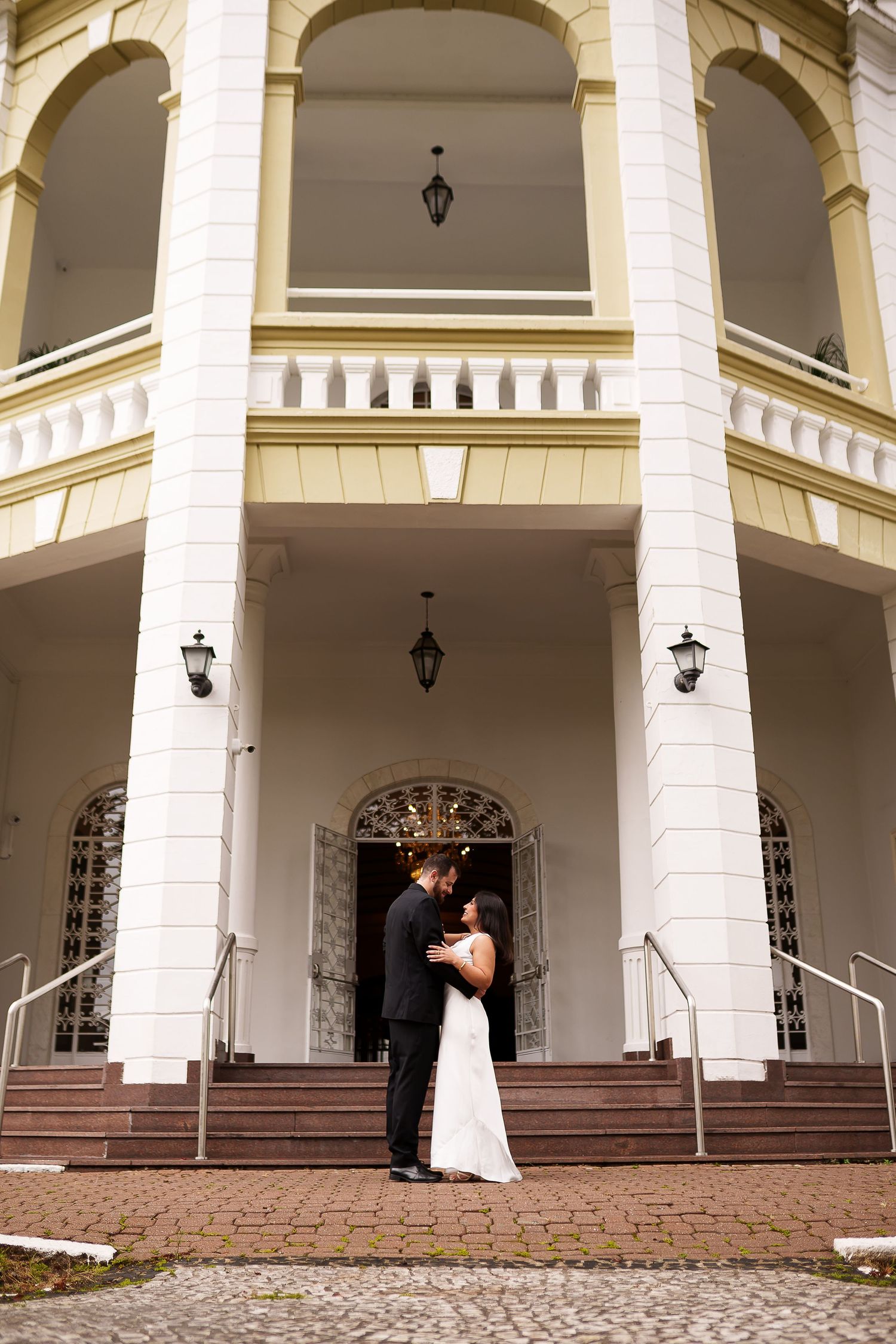 Bride and groom embracing on steps of elegant white colonial building with tall columns on wedding day.