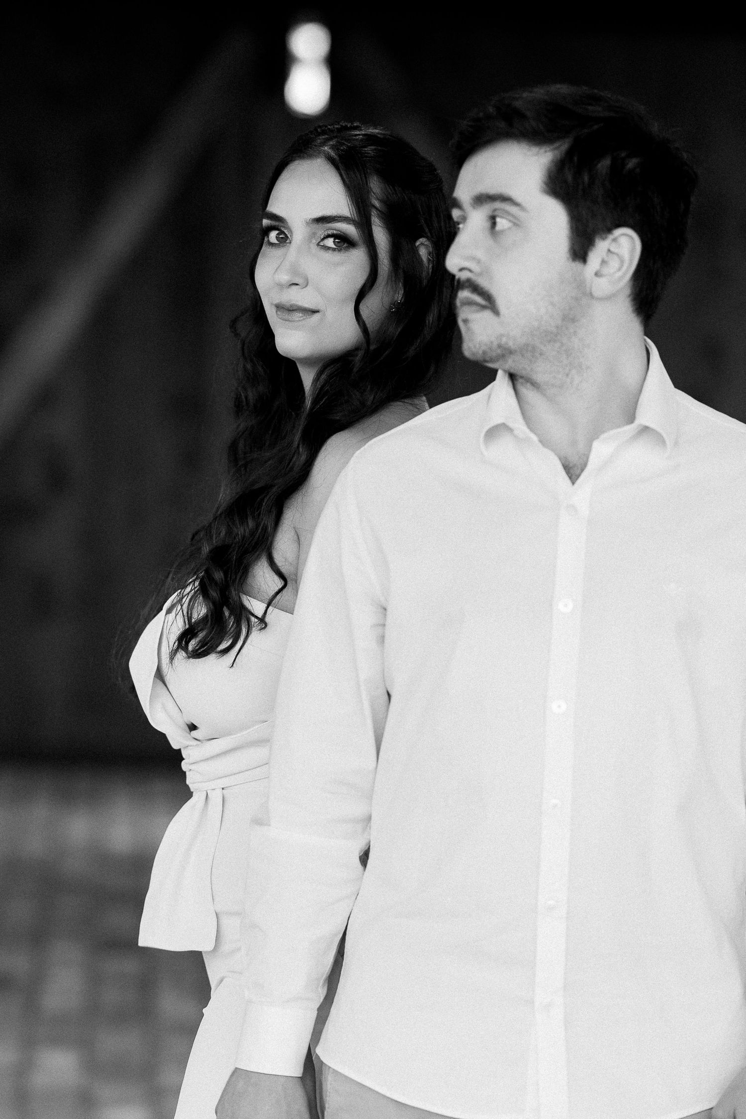 Black and white portrait of a couple in white outfits, woman with long wavy hair looking at camera, man beside her.