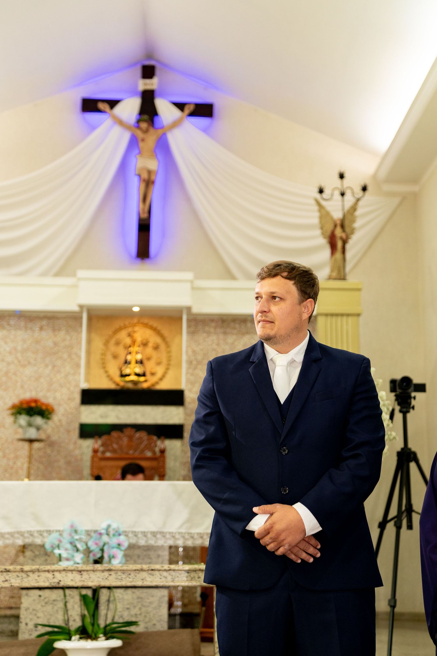 Man in navy suit standing in Catholic church with crucifix and altar in background.