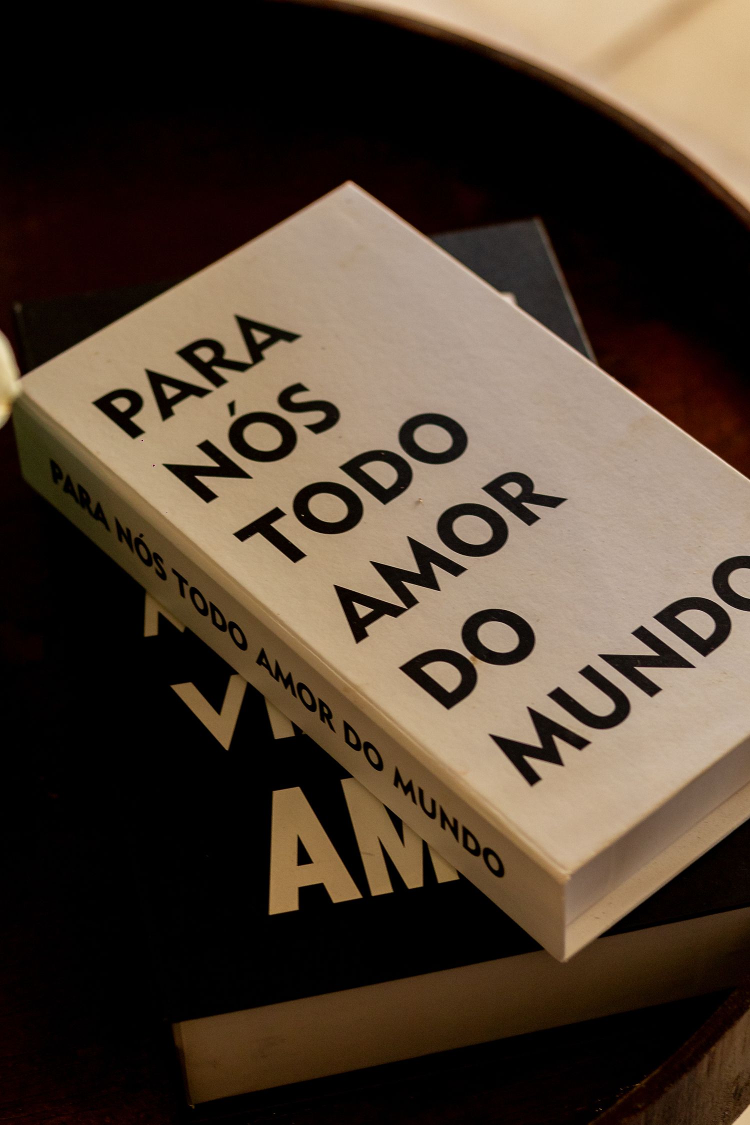 Two stacked books titled Para Nos Todo Amor Do Mundo displayed on a dark wooden tray.