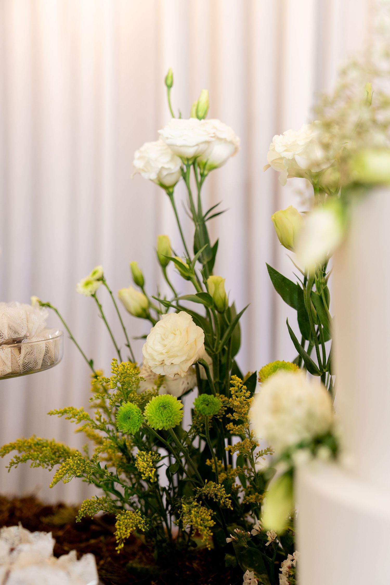 Elegant white roses and green flowers arrangement beside a white wedding cake at a reception.