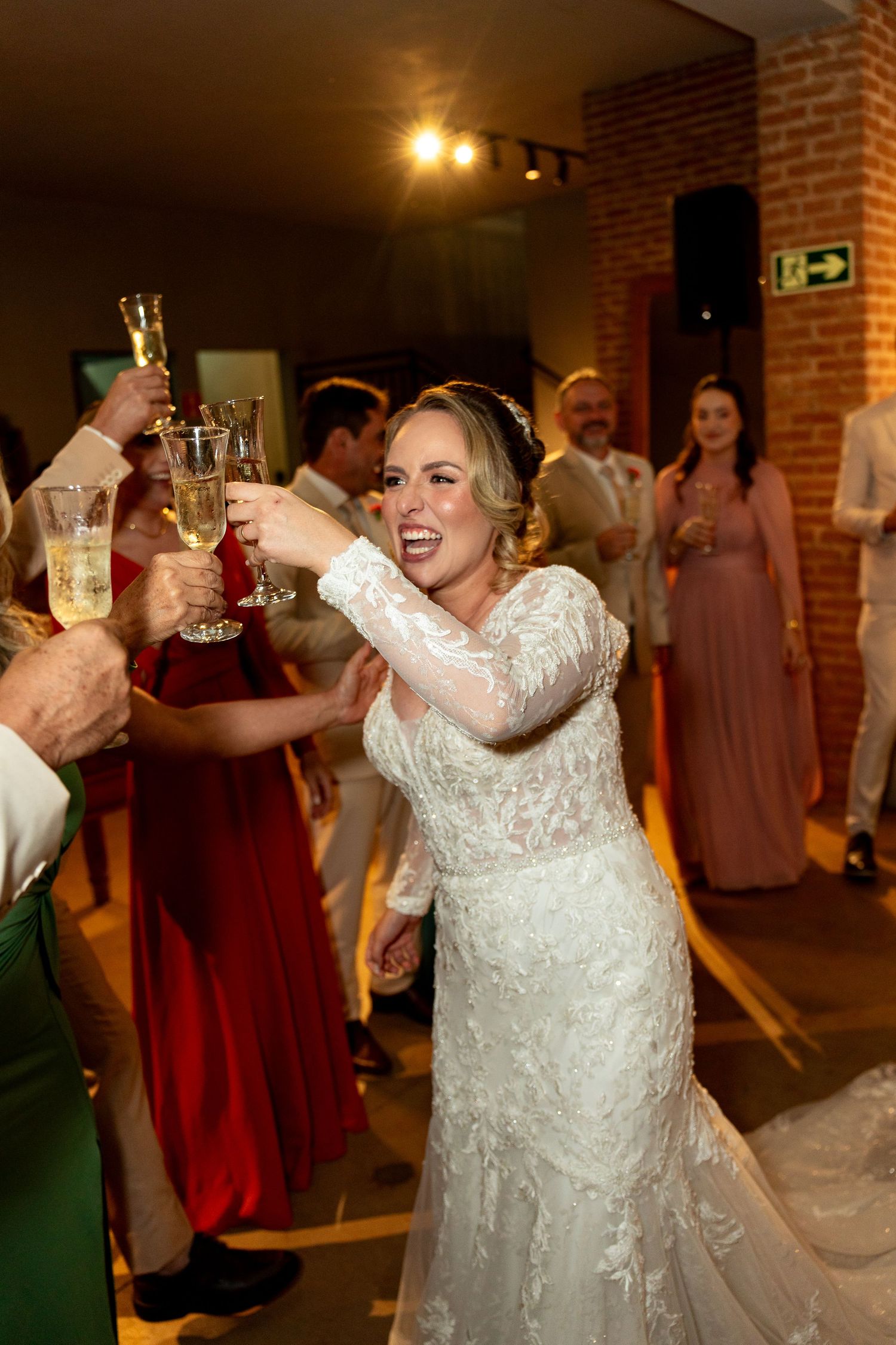 Bride in lace wedding gown toasting champagne with guests at wedding reception celebration.