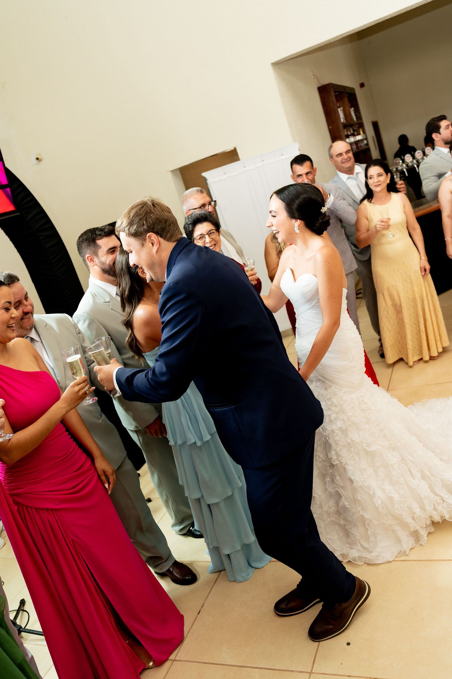 Bride and groom dancing joyfully at wedding reception surrounded by guests in formal attire.