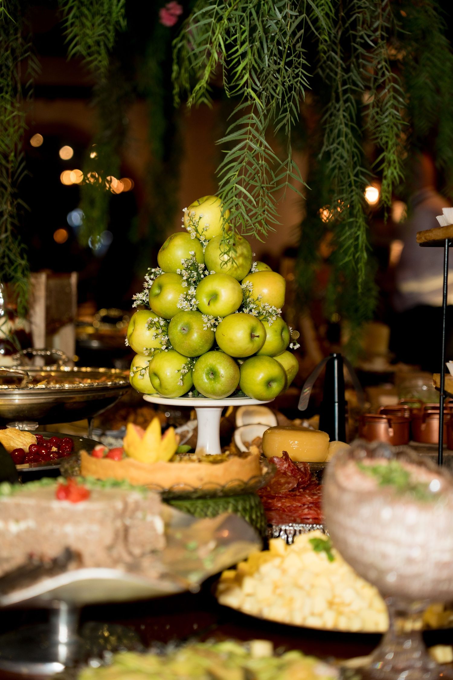 Elegant buffet display with a pyramid of green apples on a white stand, surrounded by various dishes and hanging greenery.