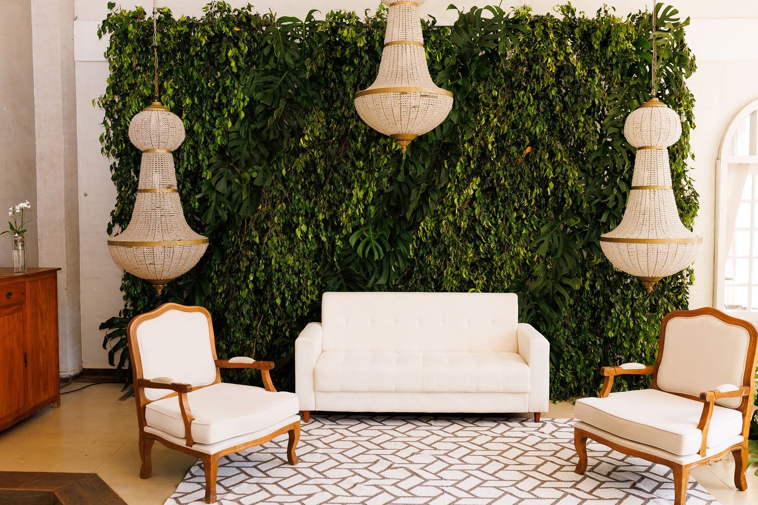 Elegant lounge seating area with white sofa, chairs, chandelier pendants, and lush green living plant wall backdrop.