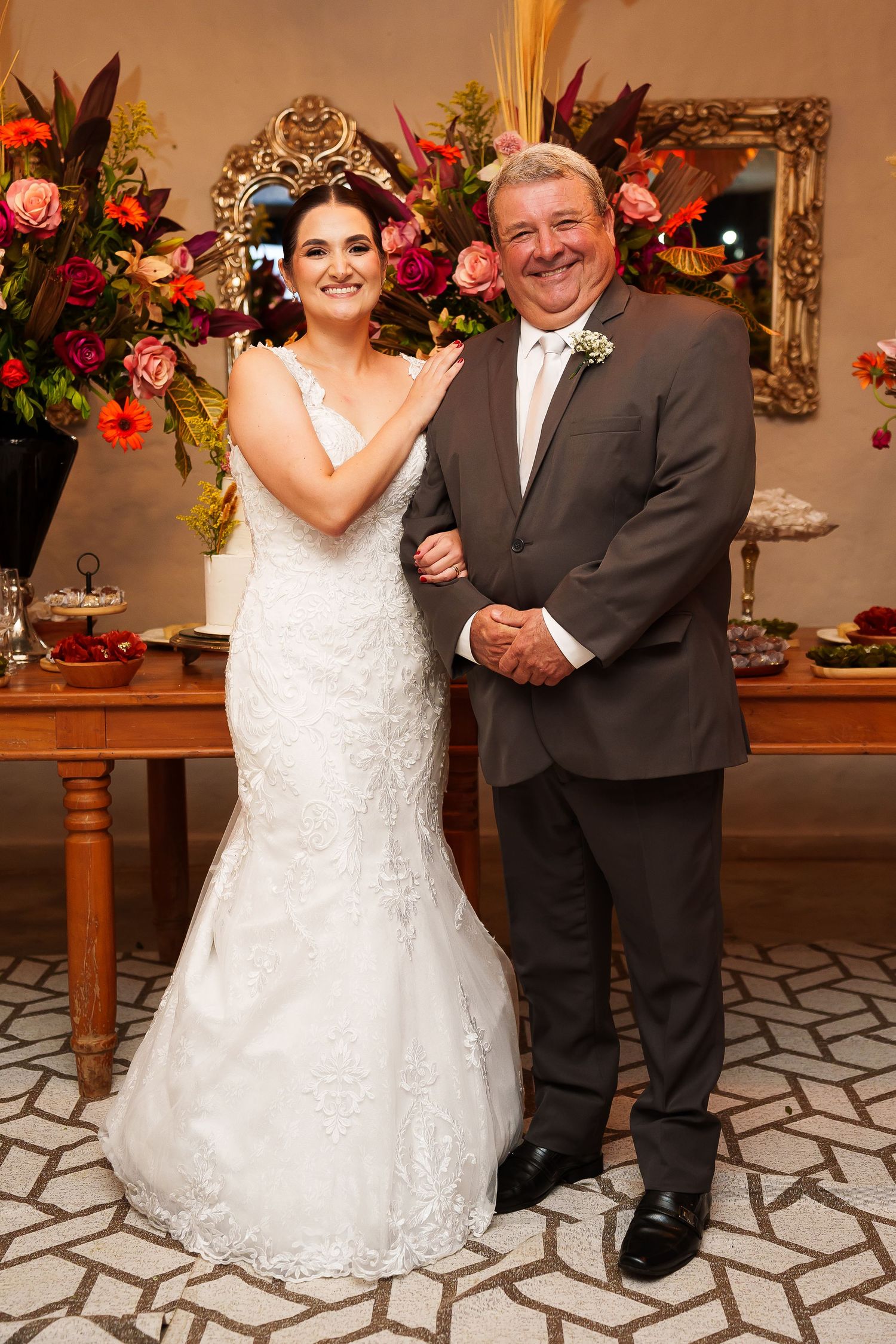Bride in white lace mermaid gown poses with man in gray suit at elegant wedding reception.