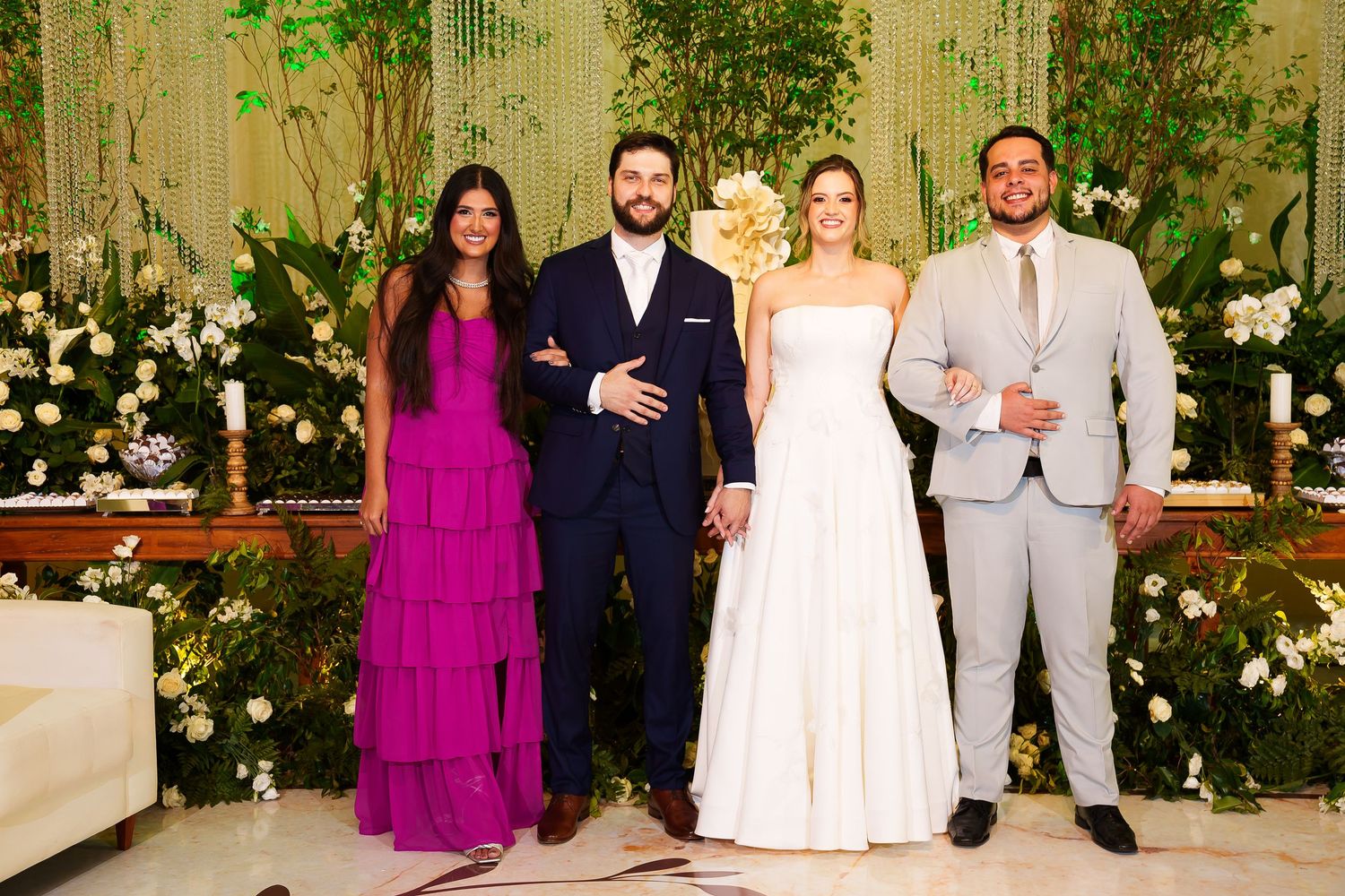 Wedding party of four posing elegantly, bride in white gown, groom in navy suit, guests in magenta dress and gray suit.