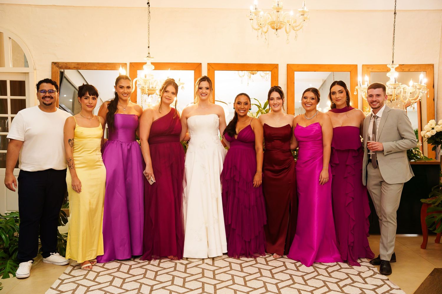 Bride in white gown poses with bridesmaids in colorful purple and yellow dresses at elegant wedding reception.