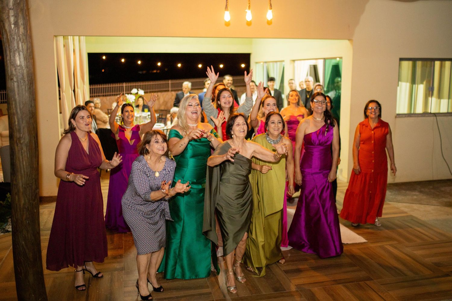 A group of women in colorful formal gowns celebrate together at an elegant indoor event venue.