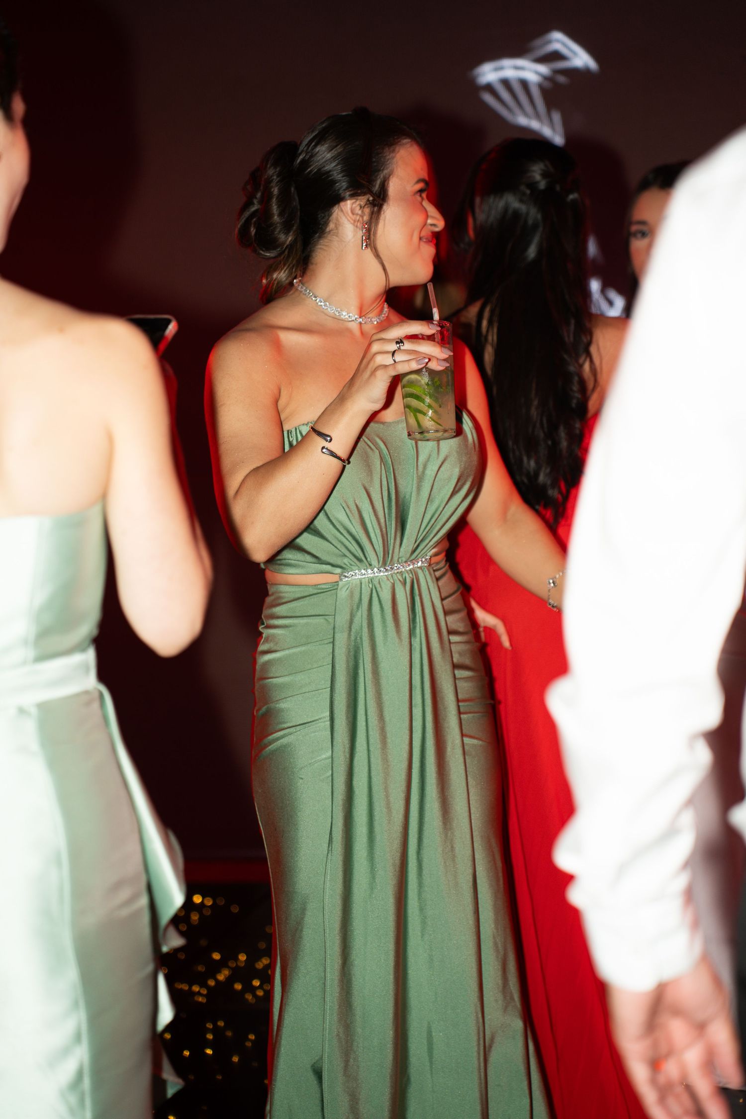 Woman in elegant green gown holding a cocktail at a formal party event.